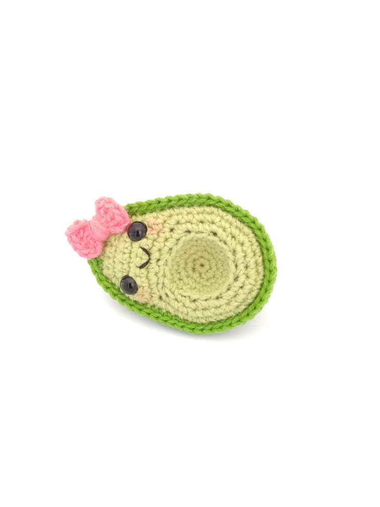 amigurumi de aguacate niña con moño rosa acostado de lado