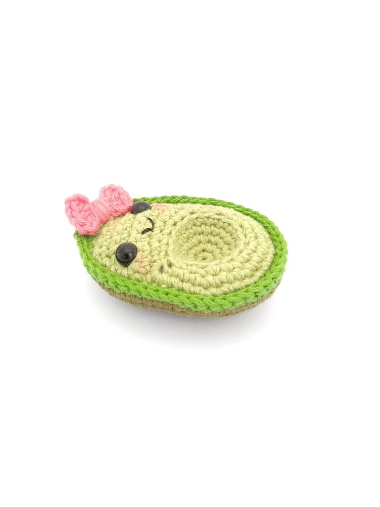 amigurumi de aguacate niña con moño rosa acostado